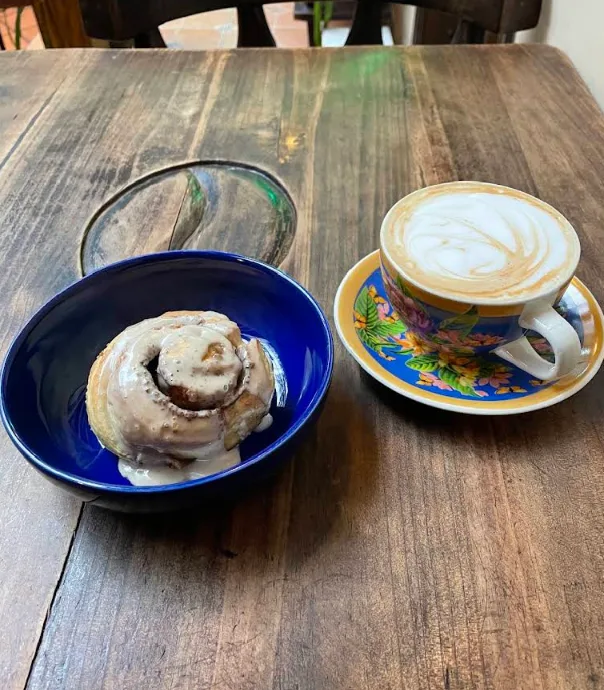 Rol de canela glaseado en plato azul con un latte
